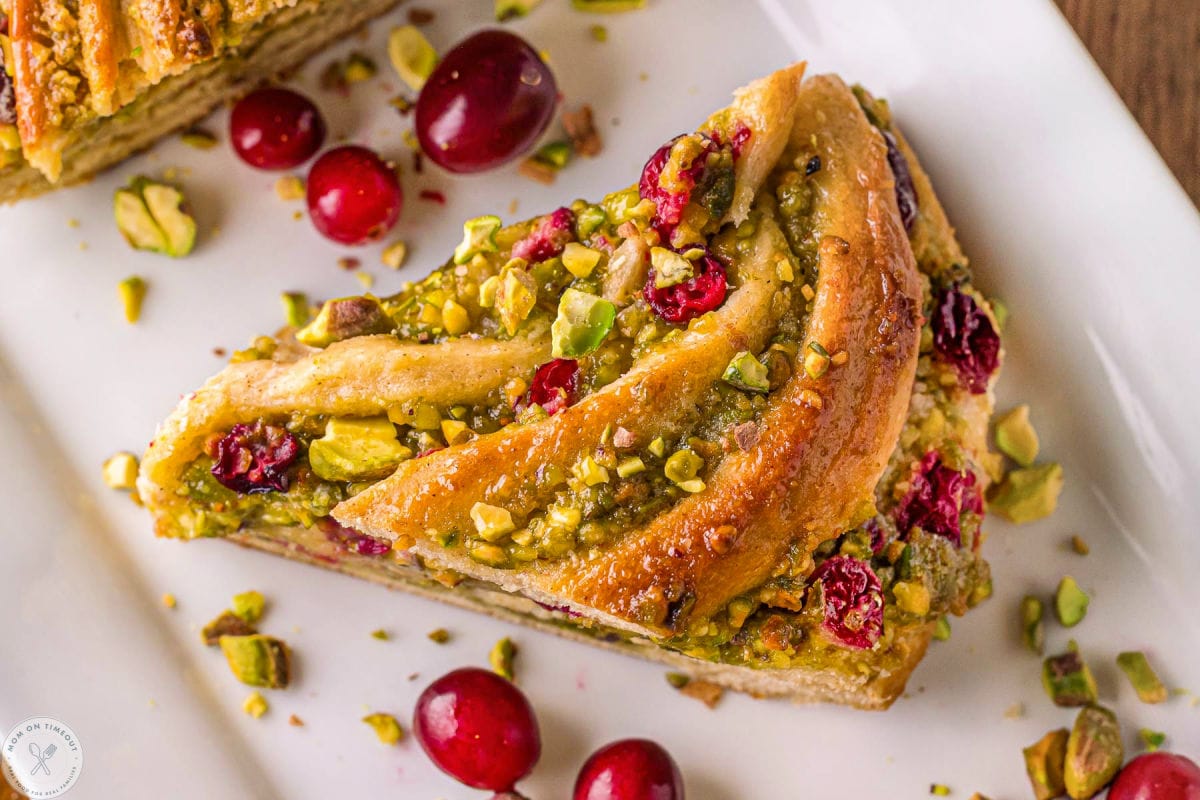 Wide shot of piece of babka bread on white tray. Shown with cranberries and pistachios.