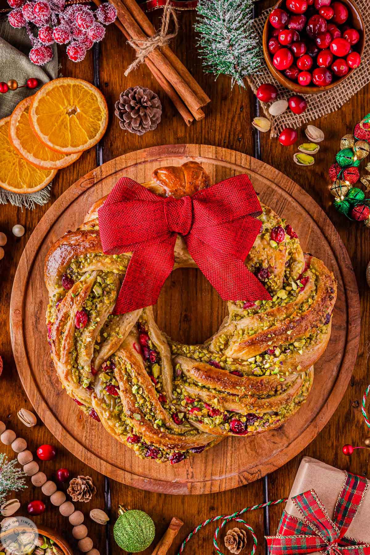 Overhead shot of cranberry pistachio babka shaped as a wreath sitting on round wood board.