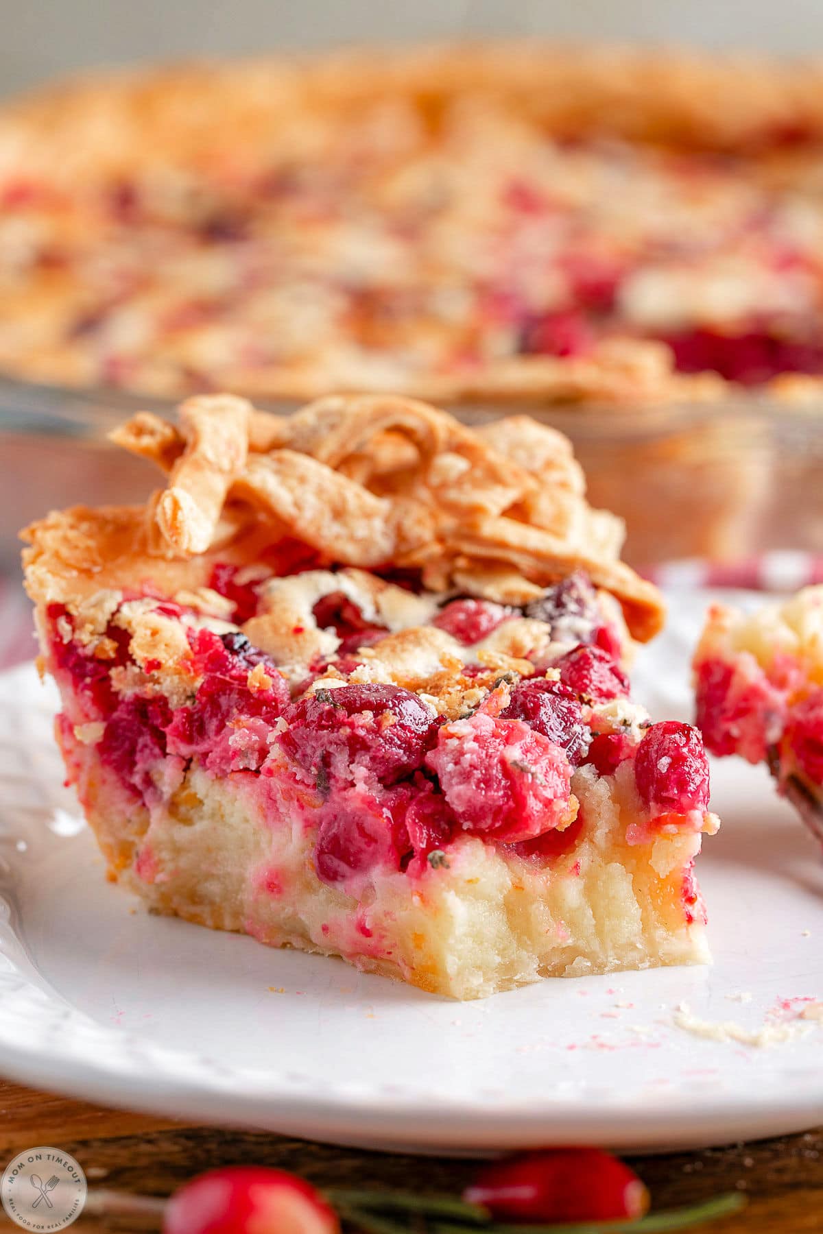 Piece of custard cranberry pie on white plate with bite taken off of end.
