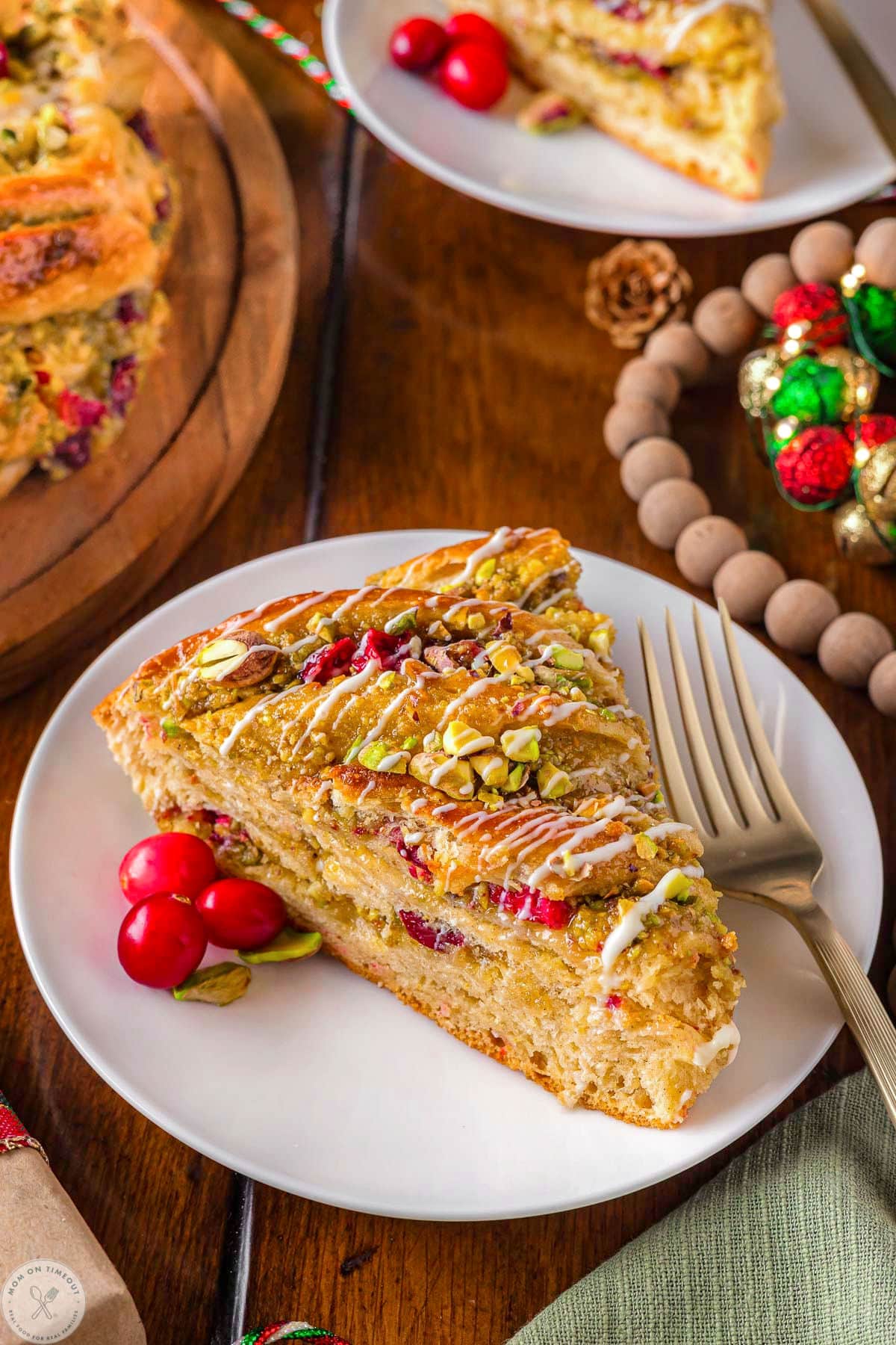 Piece of holiday babka bread on white round plate made with cranberries and pistachios.