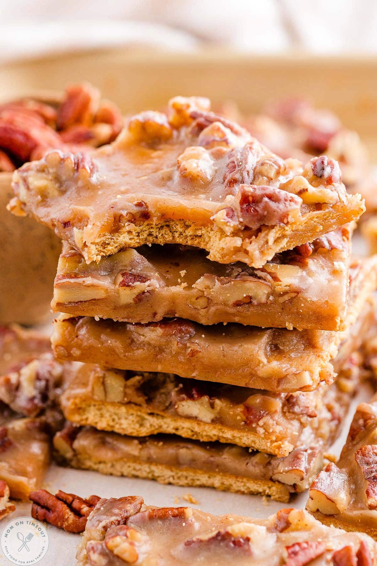 Stack of pecan pie bark with top piece a bite is taken. Pecans can be seen in the background.