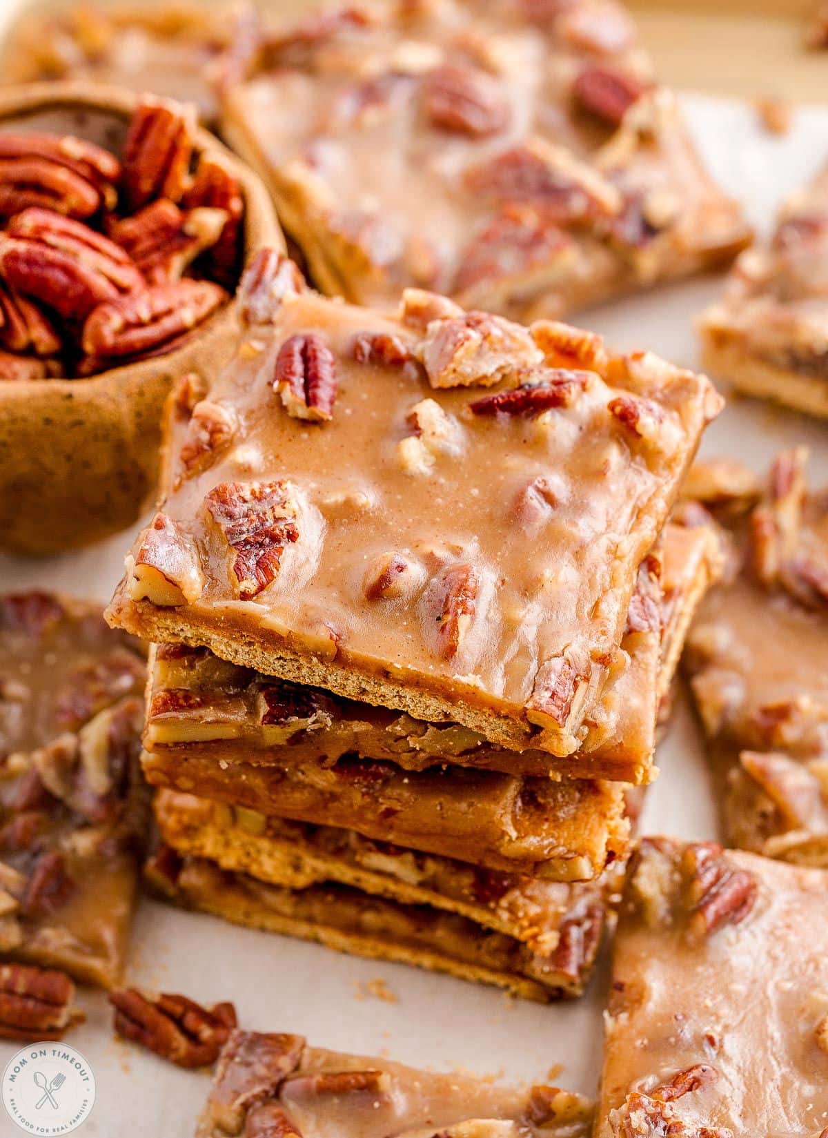 Angled overhead shot of pecan pie bark next to a bowl of pecans.