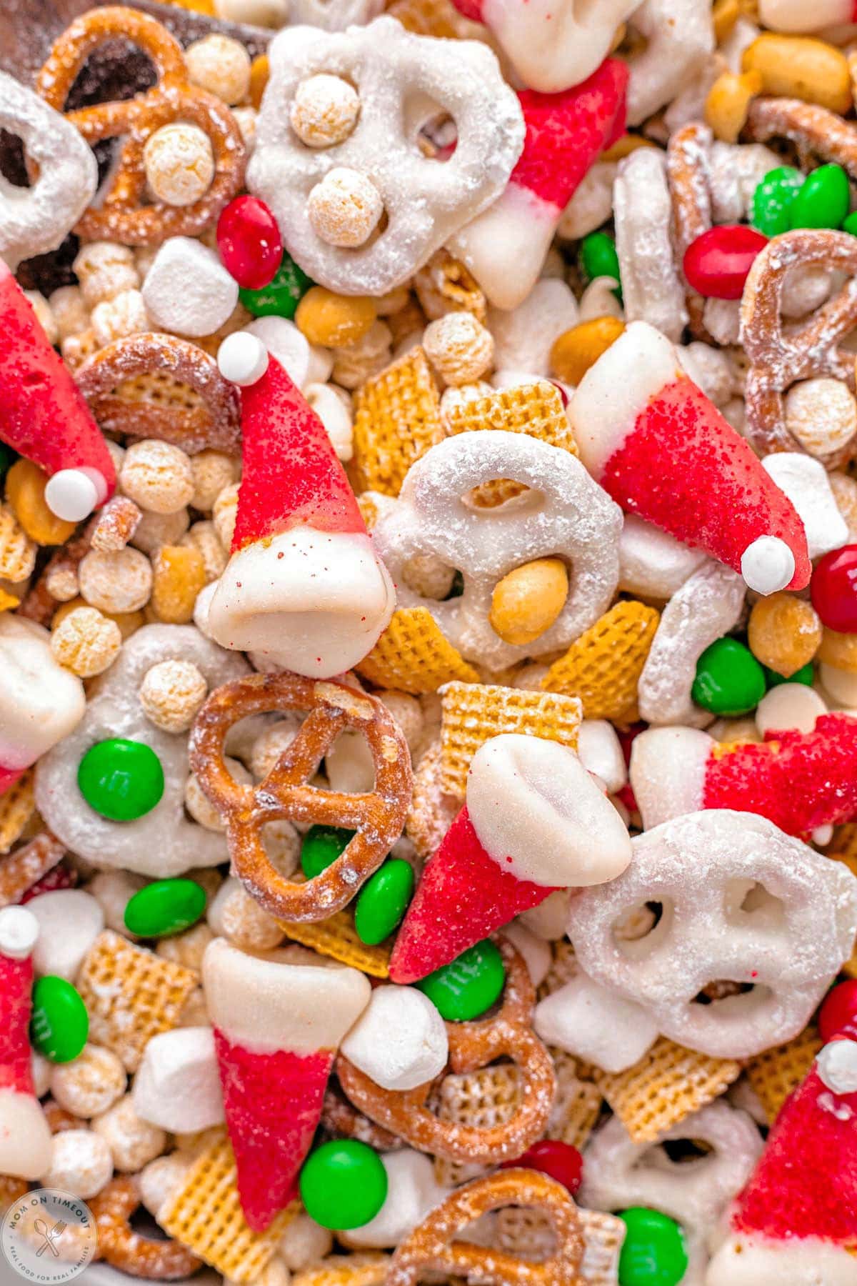 Close up shot of santa hat christmas snack mix including cereal, pretzels and candy.