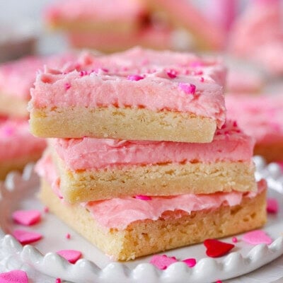 Three sugar cookie bars decorated for valentine's day stacked on white plate.