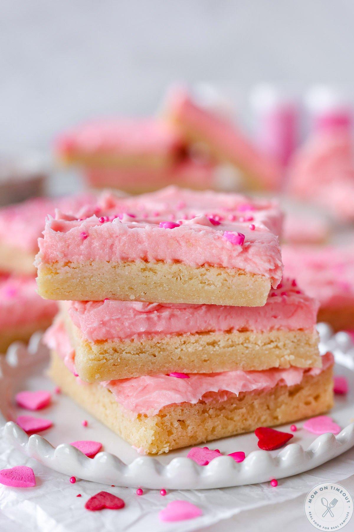 Three sugar cookie bars decorated for valentine's day stacked on white plate.