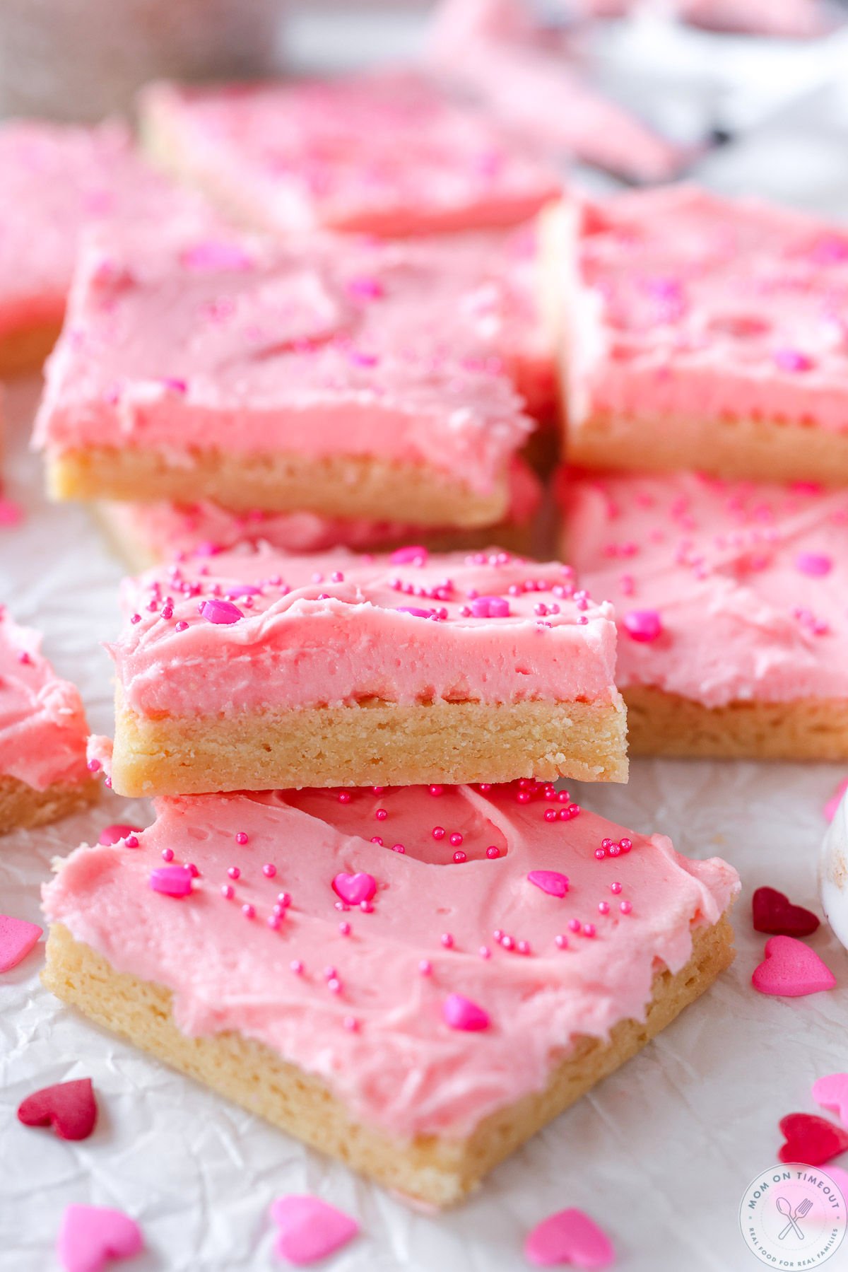 Sugar cookie bars laid out on white parchment. Bars have pink frosting and sprinkles.