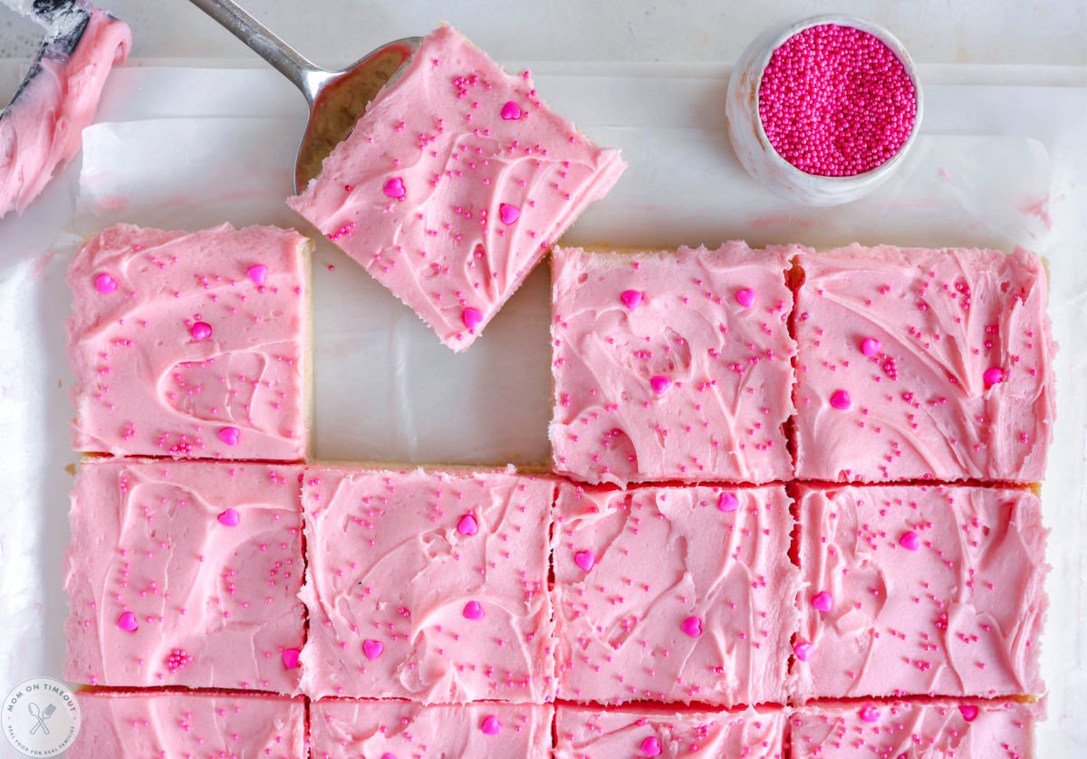 Valentine's Day Sugar Cookie Bars cut into squares on white parchment paper. One bar is being lifted away.