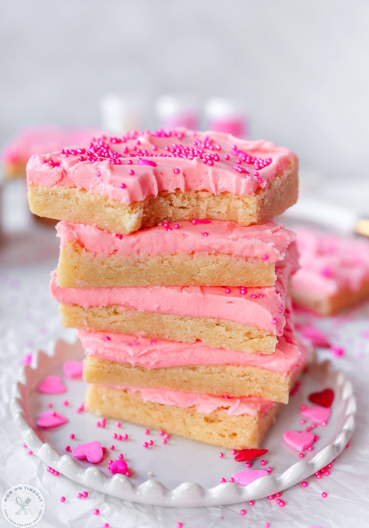 Stack of four sugar cookie bars frosted with cherry frosting and topped with sprinkles. 