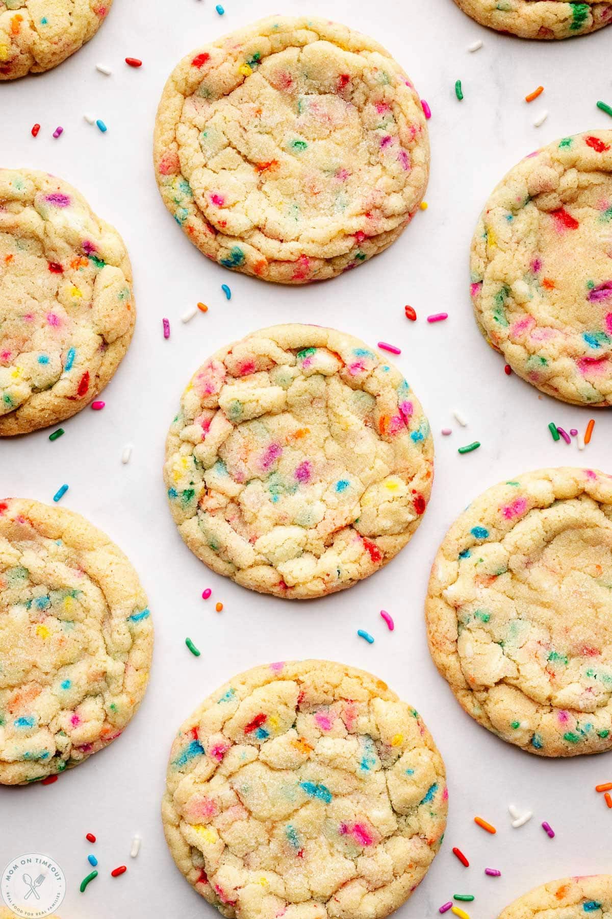 Overhead shot of sprinkle cookies spaced out on white surface with jimmies scattered about.