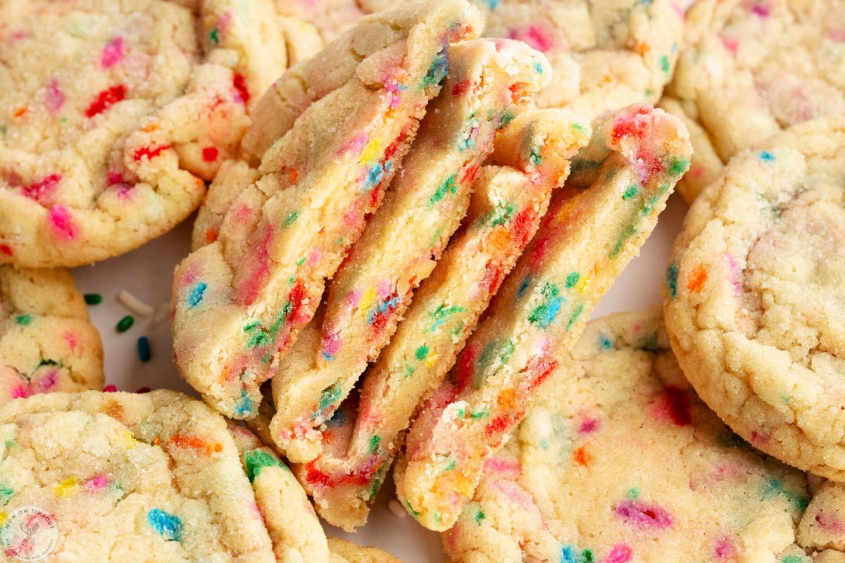 Wide shot of cookies cut in half and stacked. These cookies are sitting on even more sprinkle cookies.