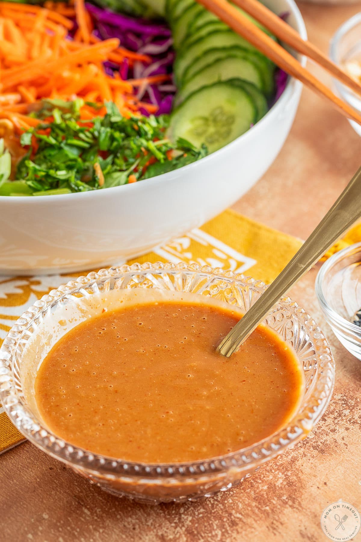 Thai peanut dressing in a small glass bowl in front of a bowl of salad.