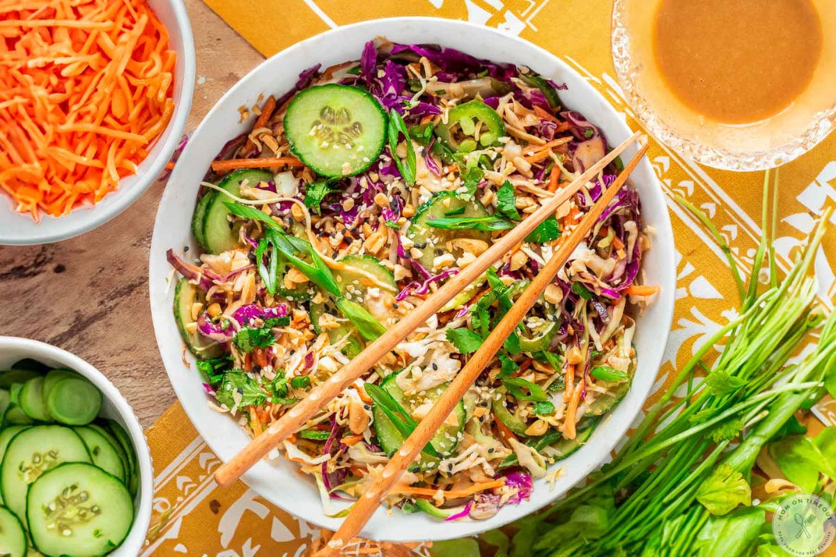 Overhead shot of large white bowl with summer thai salad that has been tossed with peanut dressing. Two chopsticks are laid on top of the bowl.