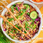 Overhead shot of large white bowl with summer thai salad that has been tossed with peanut dressing. Two chopsticks are laid on top of the bowl.
