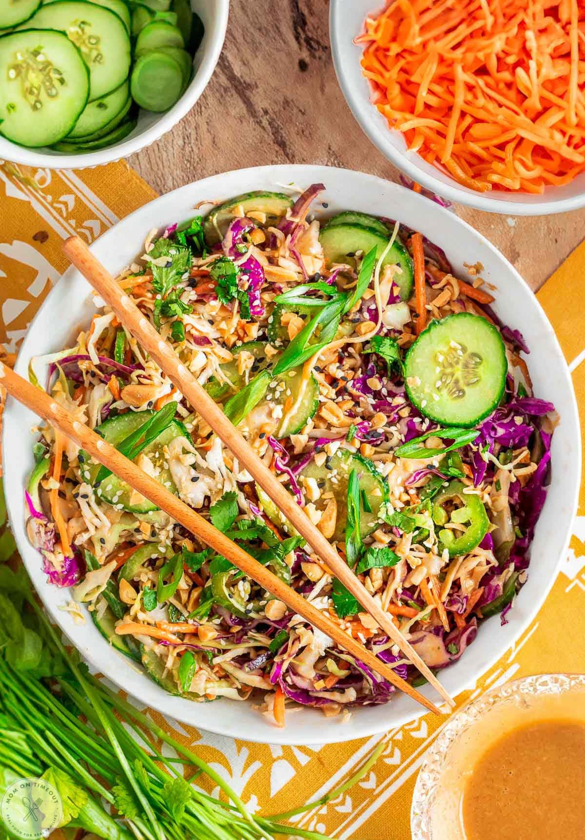 Overhead shot of large white bowl with summer thai salad that has been tossed with peanut dressing. Two chopsticks are laid on top of the bowl.