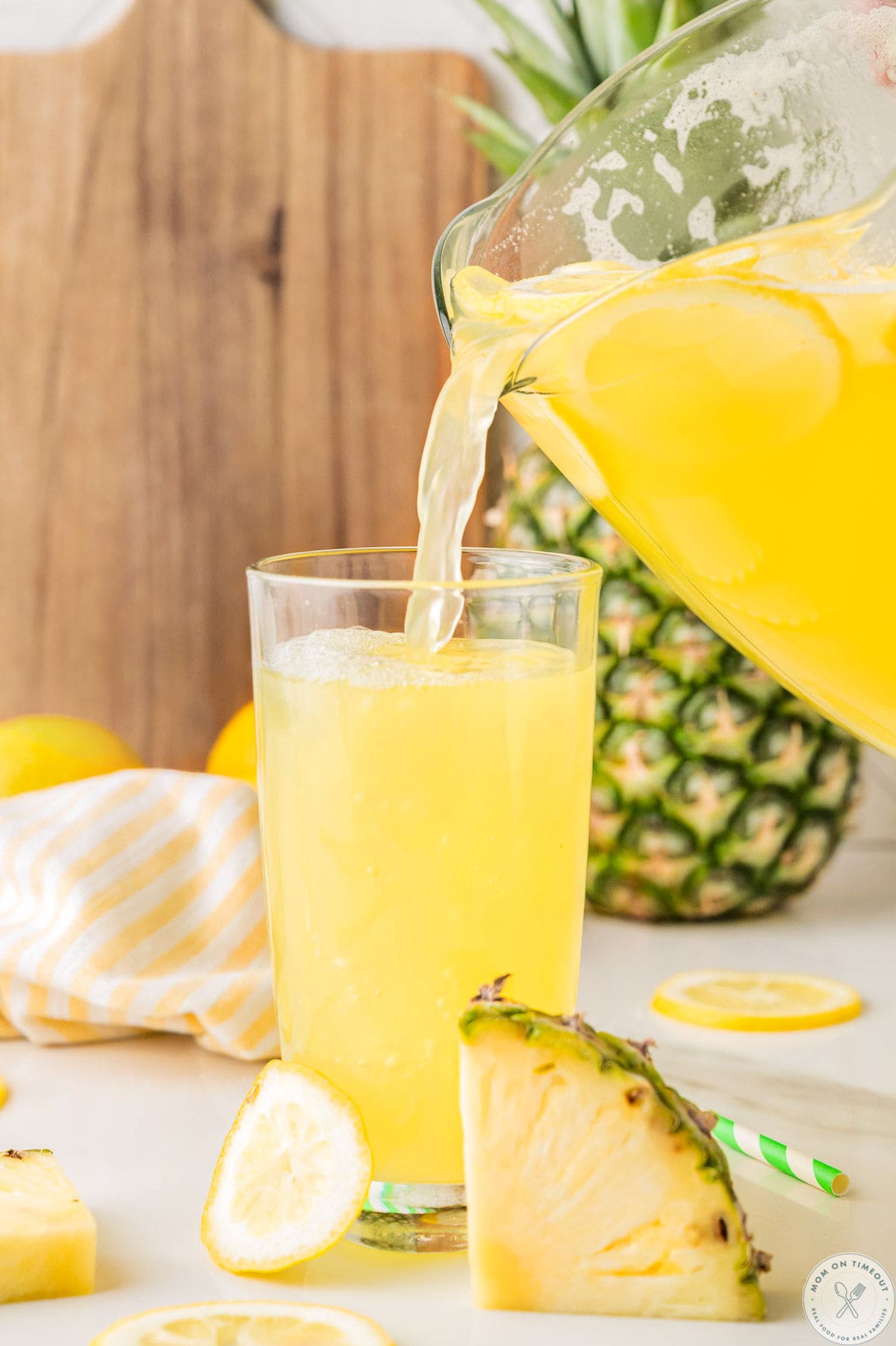 Pineapple lemonade drink being poured from a glass pitcher to a glass.