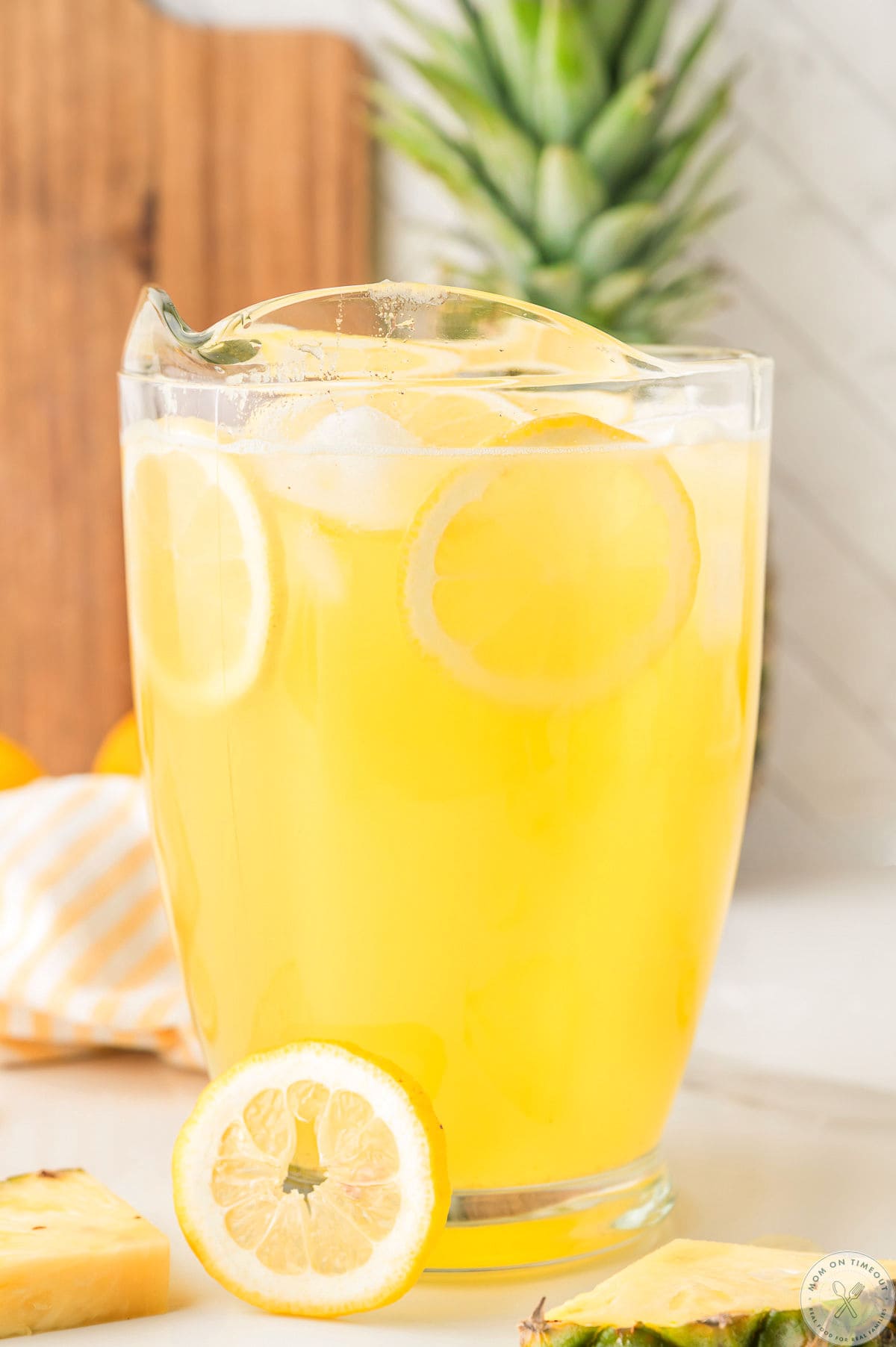 Glass pitcher filled with pineapple lemonade garnished with lemon slices and pineapple wedges.