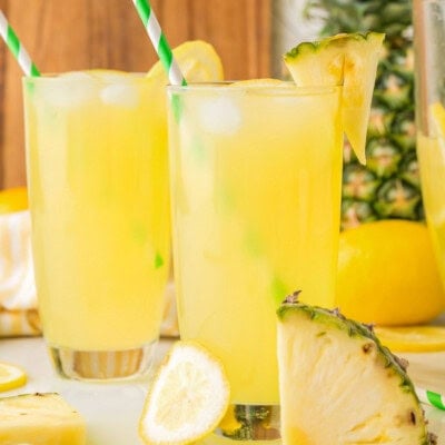 Two glasses filled with pineapple lemonade. Straws in glasses with fresh pineapple in the background.