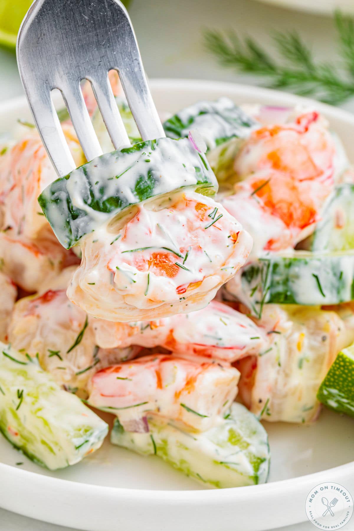 Creamy cucumber shrimp salad in bowl with fork piercing one piece of cucumber and shrimp.