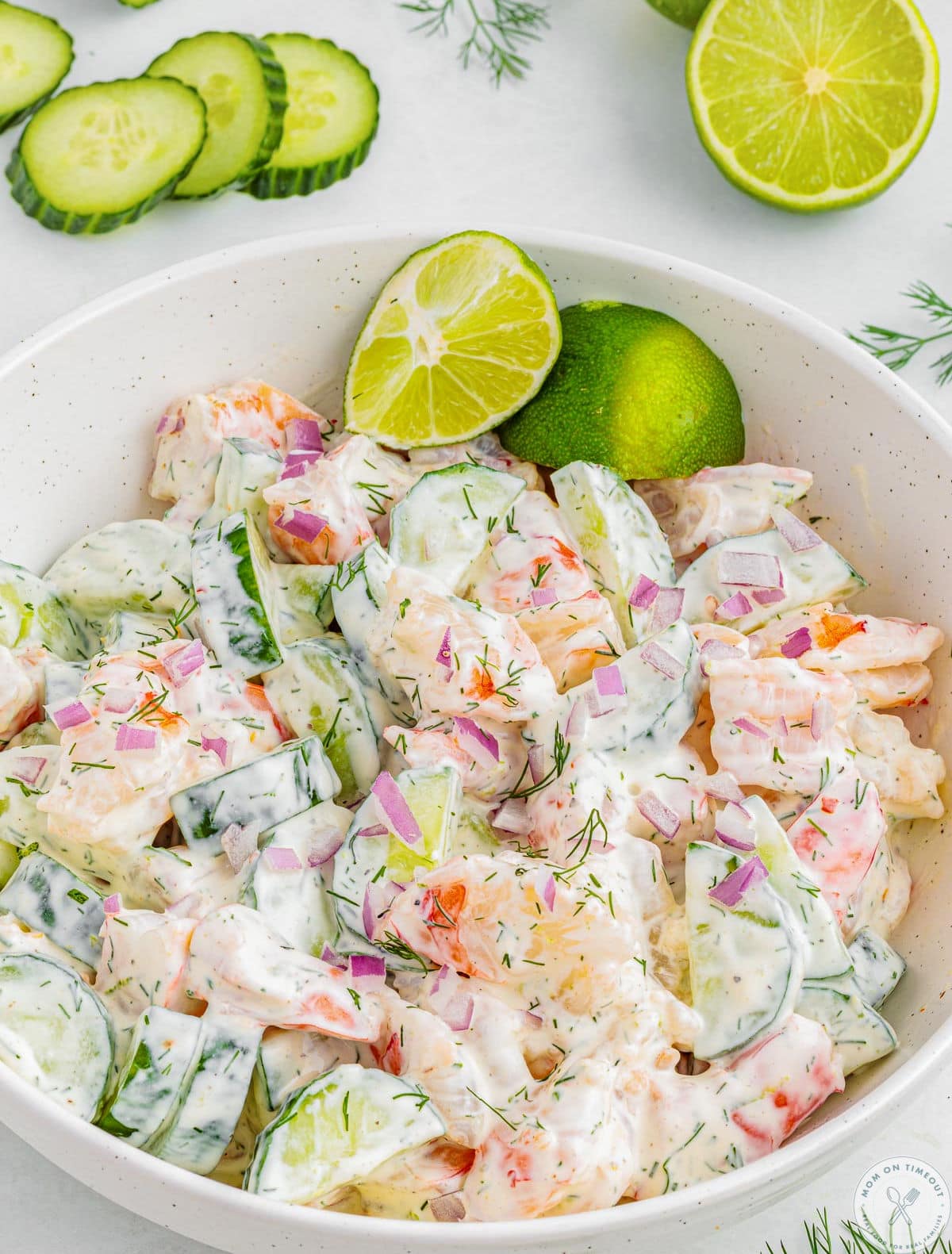 Shrimp cucumber salad in shallow white bowl garnished with lime wedges. Serving spoon sat off to the side.