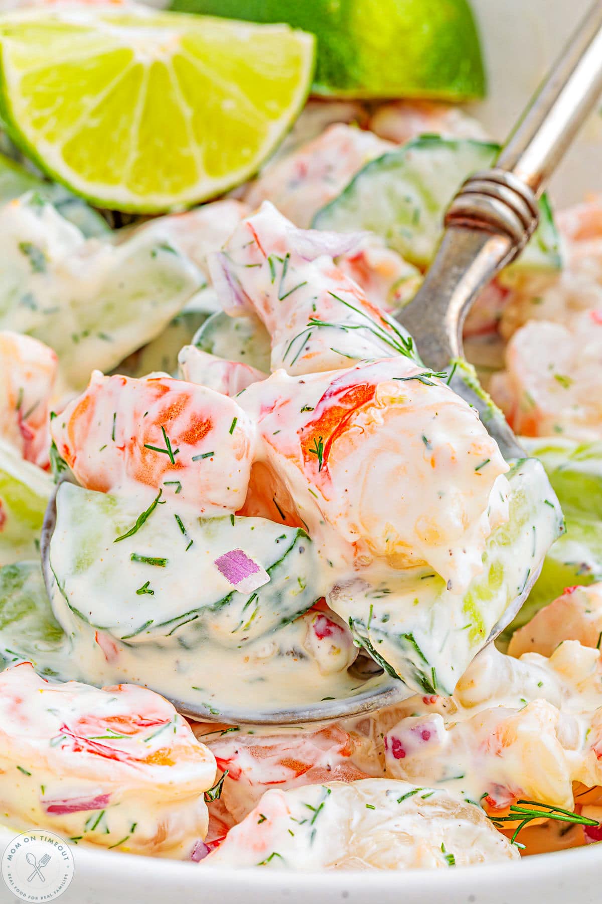 Large serving spoon with a scoop of cucumber shrimp salad being lifted away from the serving bowl.