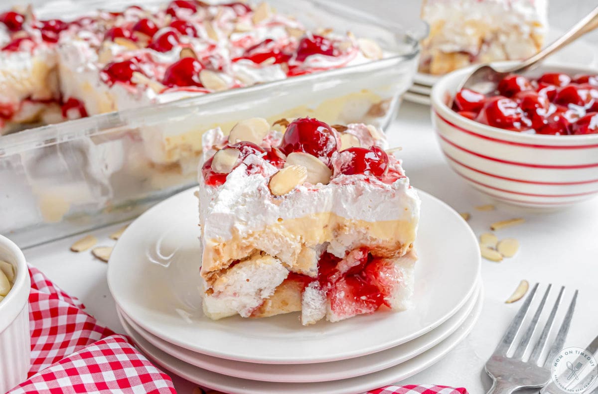 Wide shot of angel food cake with pie filling dessert served on white round plate and topped with cherry pie filling and almonds.