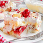 Layered heaven on earth cake recipe plated on white plate with fork off to the side. Bright red cherries and almonds adorn the cake.