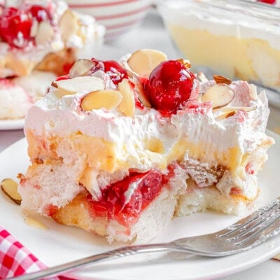 Layered heaven on earth cake recipe plated on white plate with fork off to the side. Bright red cherries and almonds adorn the cake.