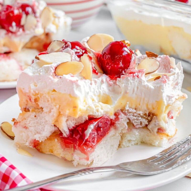 Layered heaven on earth cake recipe plated on white plate with fork off to the side. Bright red cherries and almonds adorn the cake.