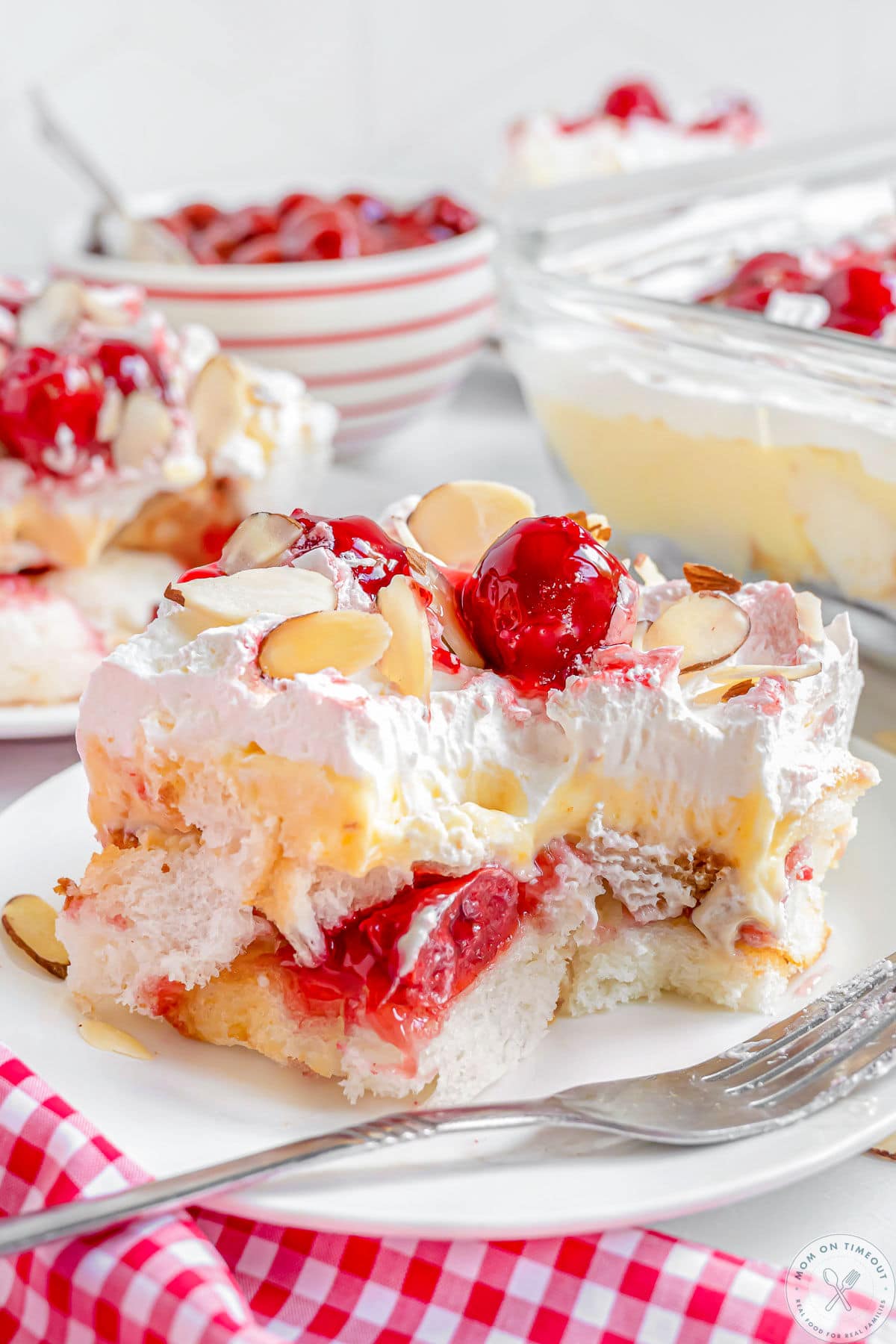 Layered heaven on earth cake recipe plated on white plate with fork off to the side. Bright red cherries and almonds adorn the cake.