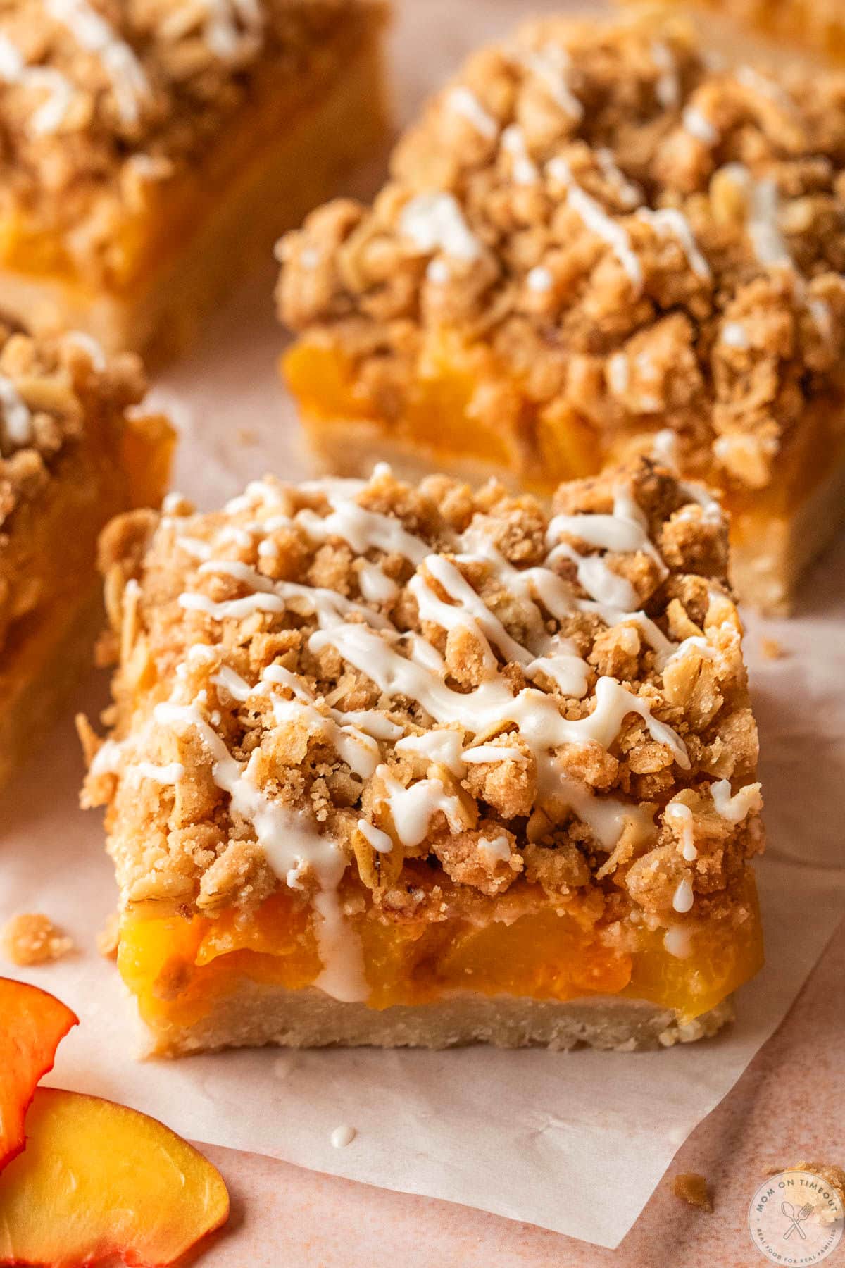 Peach Crumb Bars cut into square and sitting on parchment squares. The bars are drizzled with a glaze.