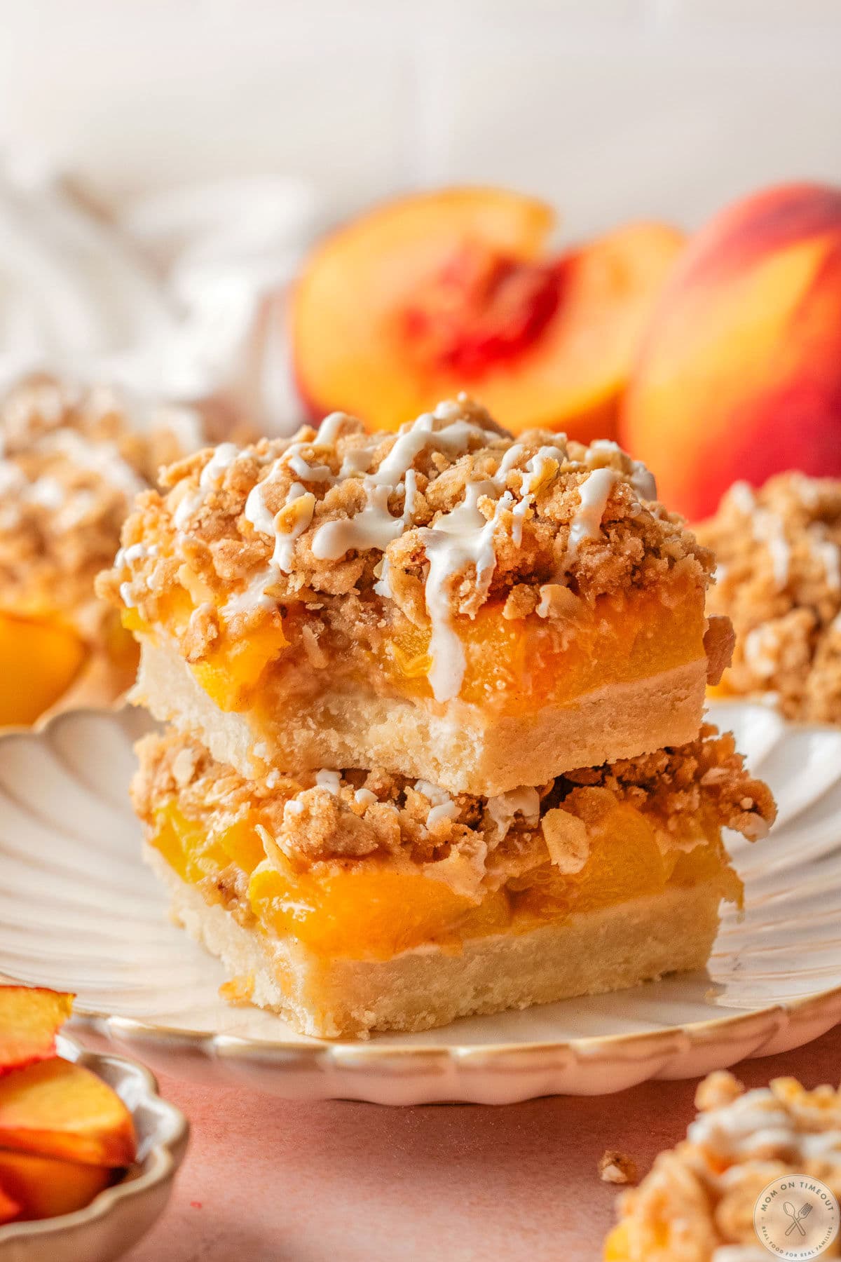 Two peach pie bars stacked on scalloped dessert plate. Topped with a drizzle and top bar has a bite taken.