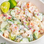 Shrimp cucumber salad in shallow white bowl garnished with lime wedges.