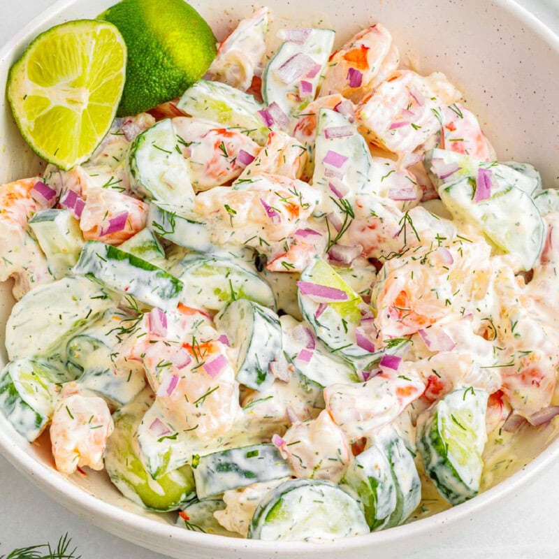 Shrimp cucumber salad in shallow white bowl garnished with lime wedges.