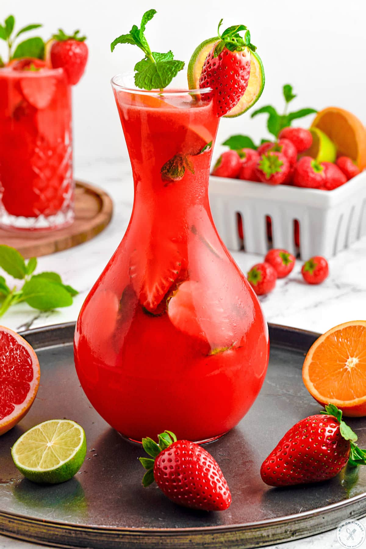 Tall glass pitcher filled with strawberry mojito recipe and garnished with fresh mint and strawberries.
