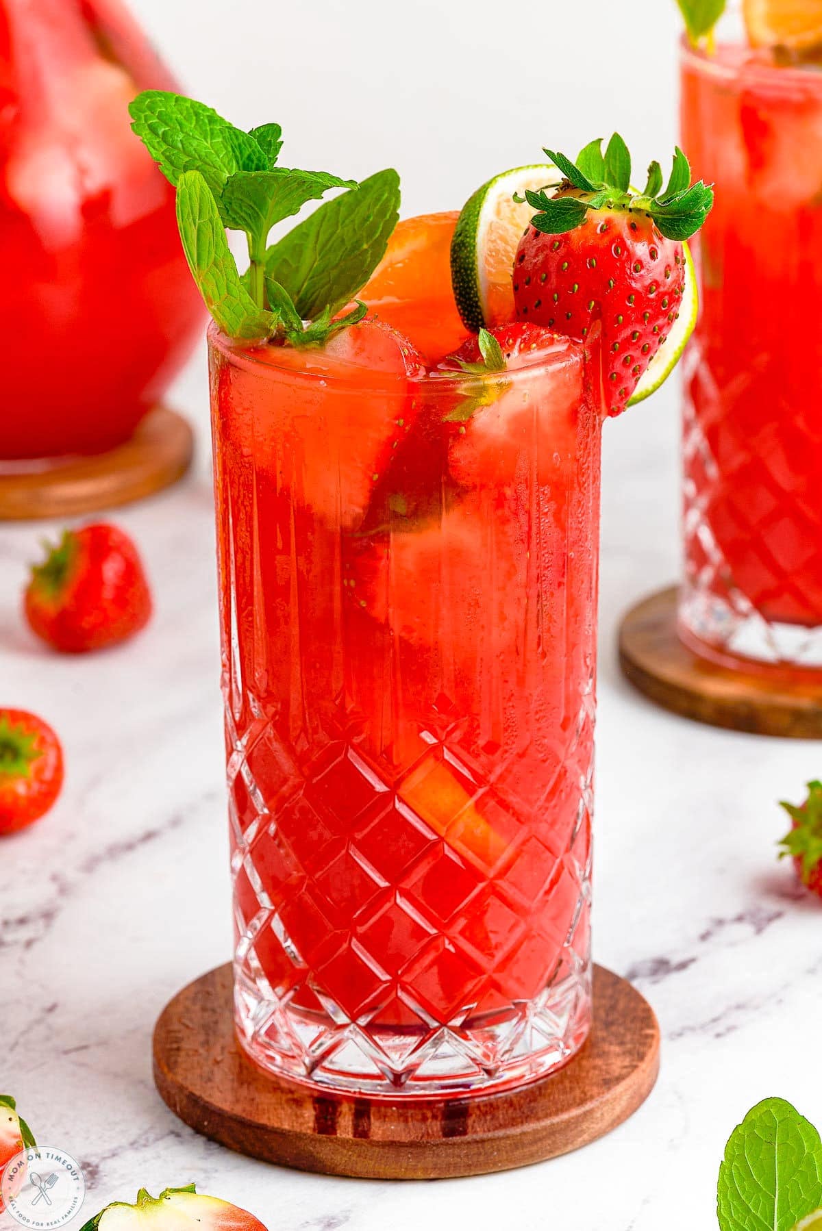 Close up of strawberry mojito in a tall glass. Garnished with mint and strawberries.