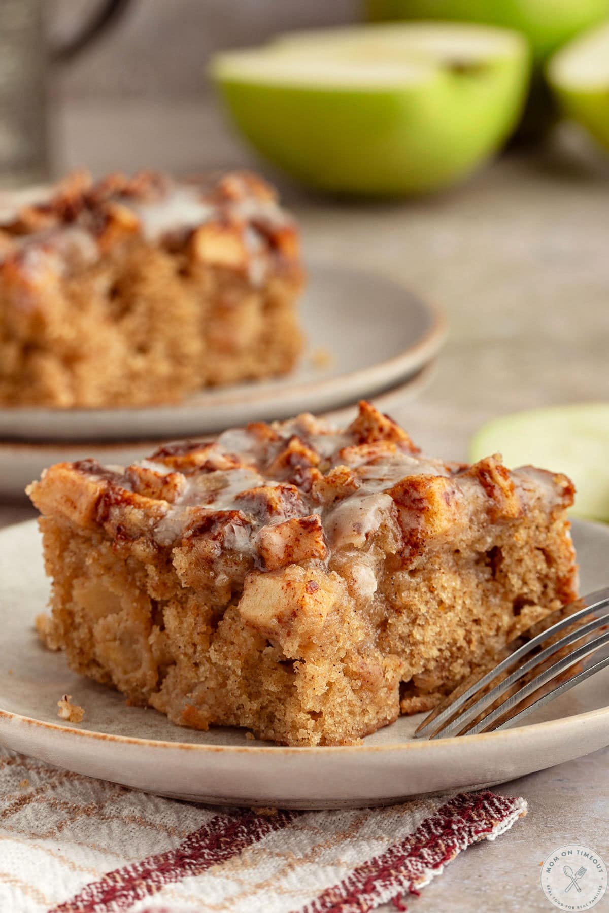 Slice of apple fritter cake on small dessert plate. Another plate can be seen in the background.