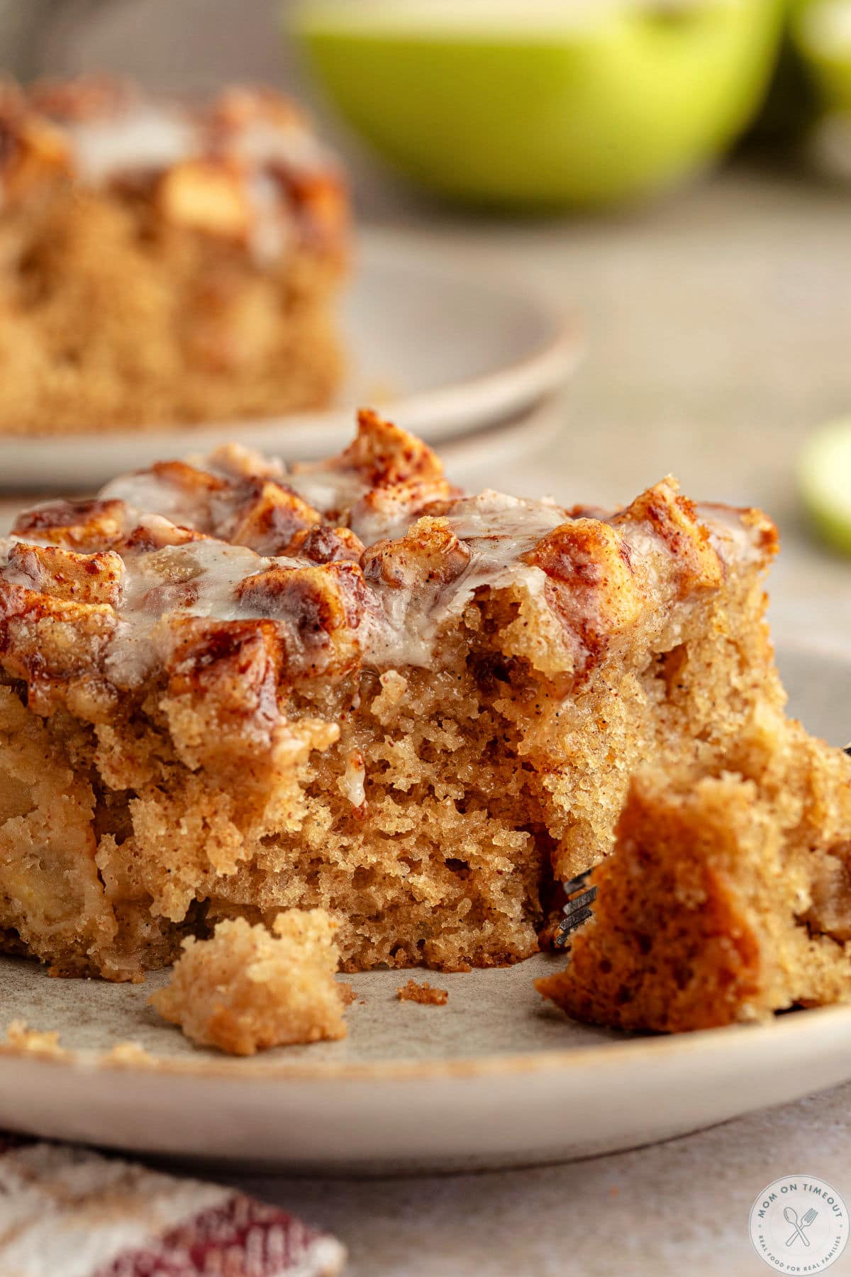 Apple fritter cake on small plate with fork that has cut off of one corner.