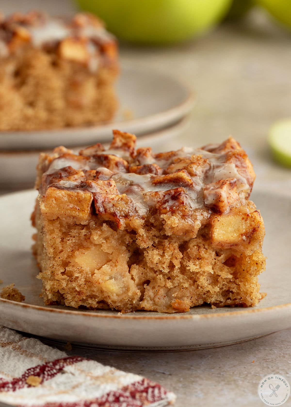 Slice of apple fritter cake on small dessert plate. Another plate can be seen in the background.