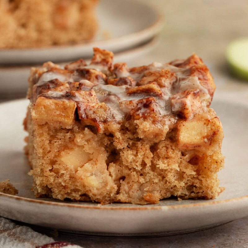 Slice of apple fritter cake on small dessert plate. Another plate can be seen in the background.