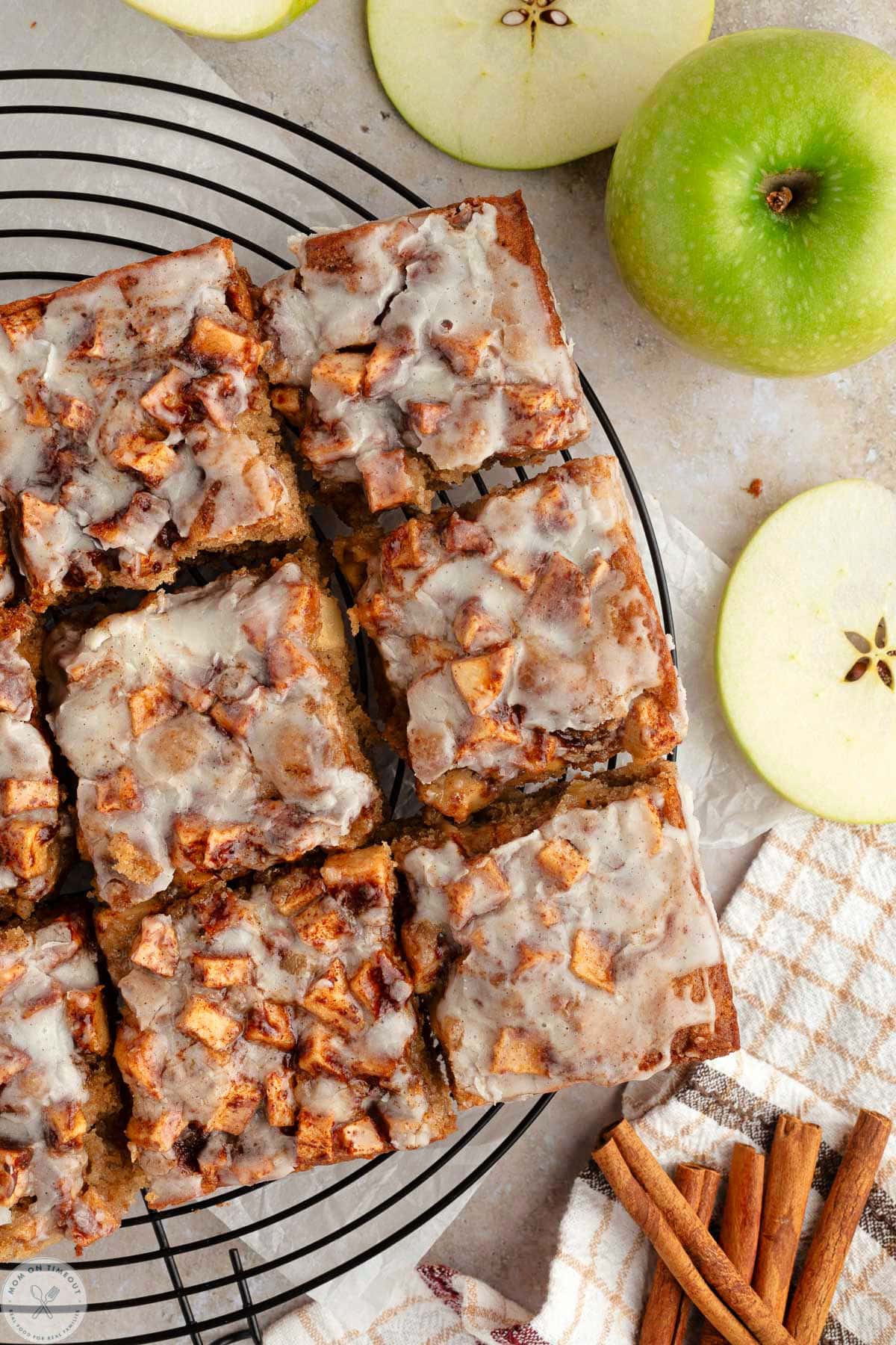 Apple fritter cake on round black cooling rack cut into squares.