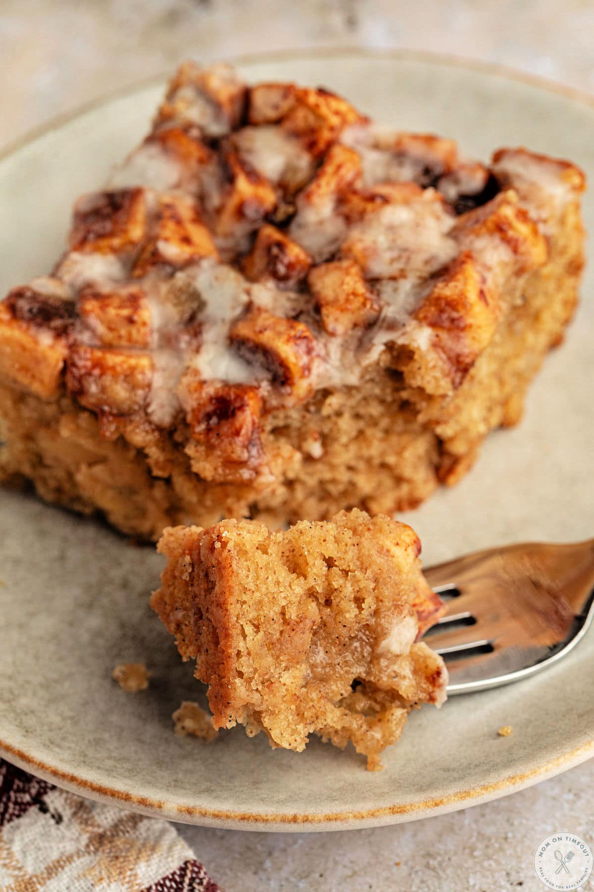 Apple fritter cake on small plate with fork that has cut off of one corner.
