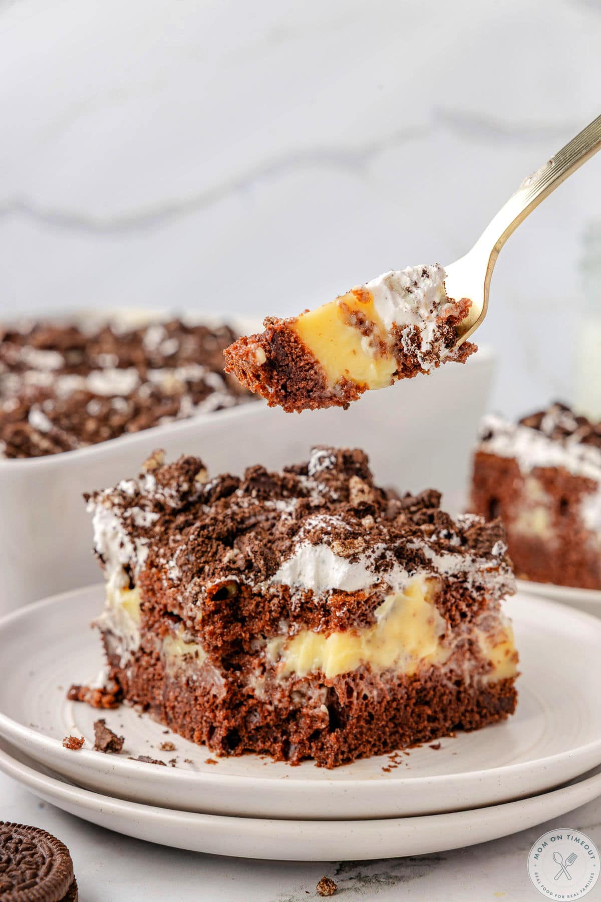 Oreo poke cake with pudding on plate and fork lifting a bite away from the cake.