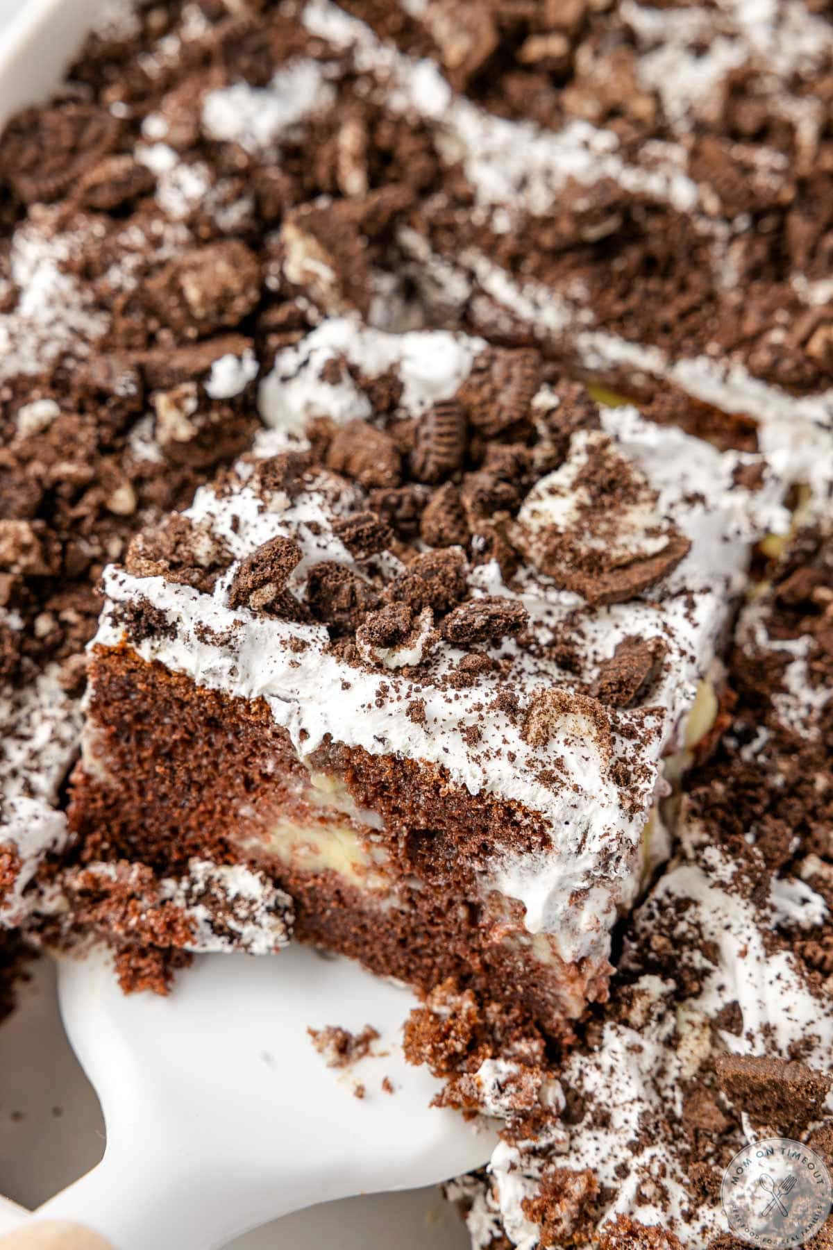 Piece of oreo poke cake being lifted from the white baking dish it was cooked in.