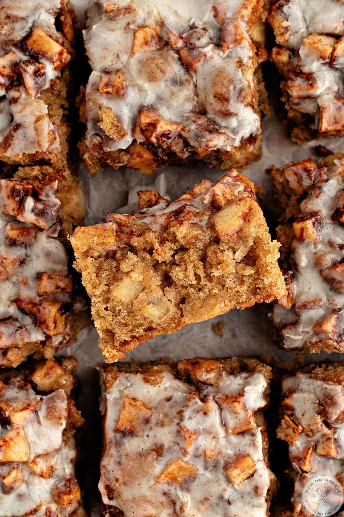 Top down view of apple fritter cake cut into 9 pieces on white parchment paper.