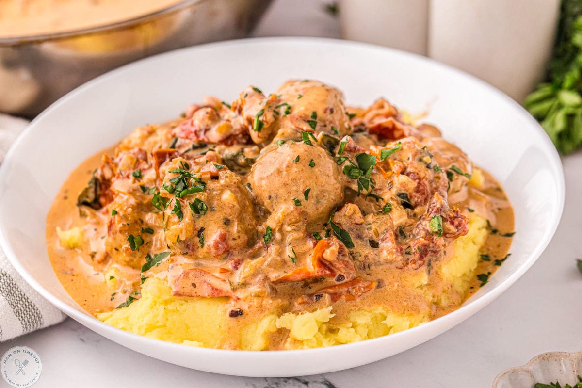 Shallow bowl filled with mashed potatoes and marry me chicken meatballs and garnished with parsley.