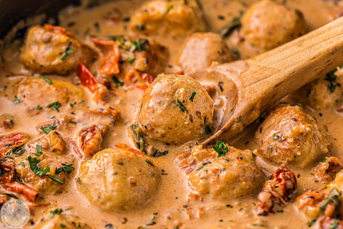 Small wood spoon scooping up chicken meatballs from skillet.