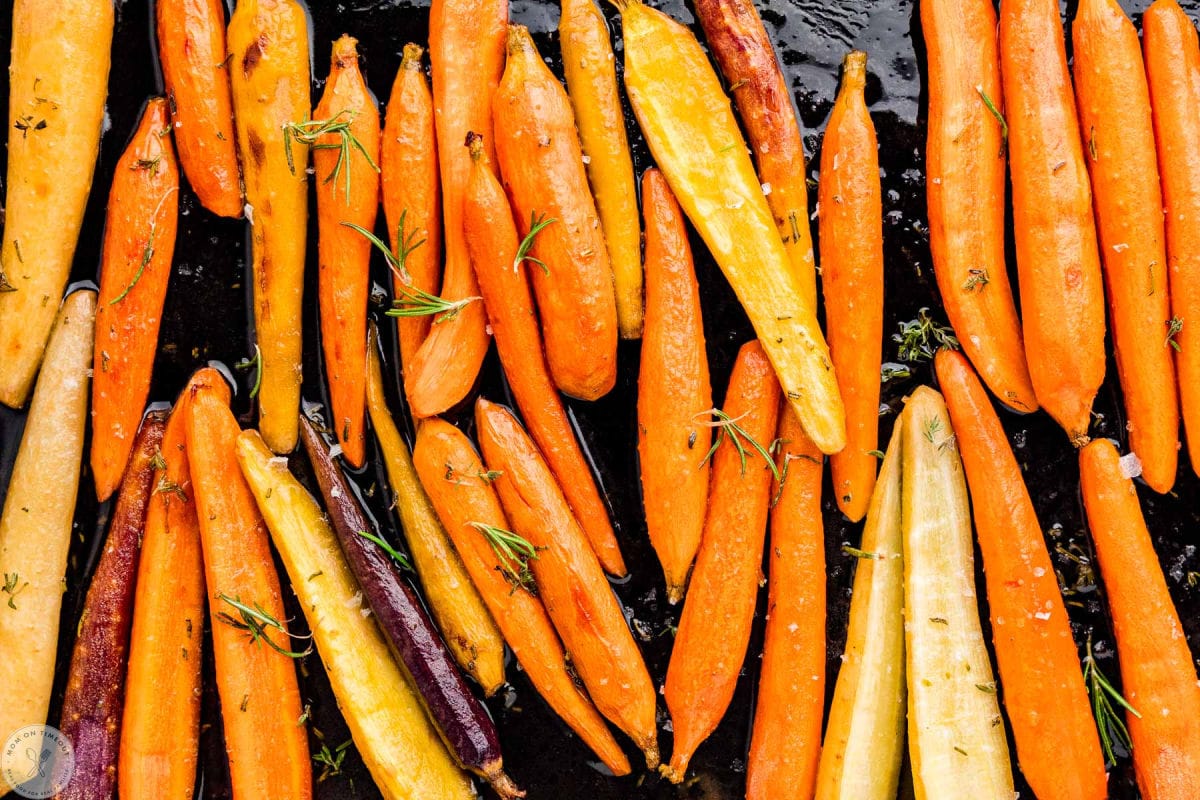 Wide, close up shot of maple cooked carrots on baking sheet.