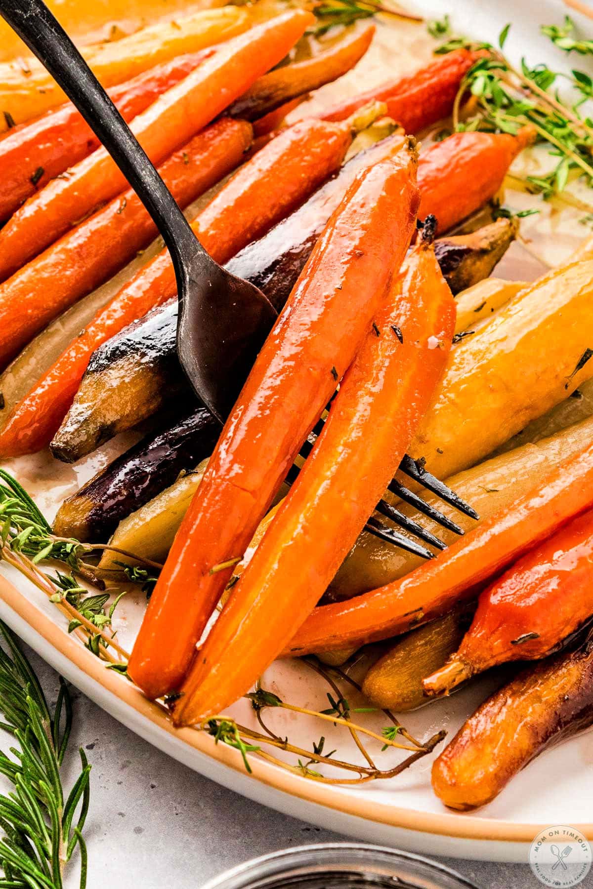 Black serving fork lifting two maple roasted carrots off of serving dish.