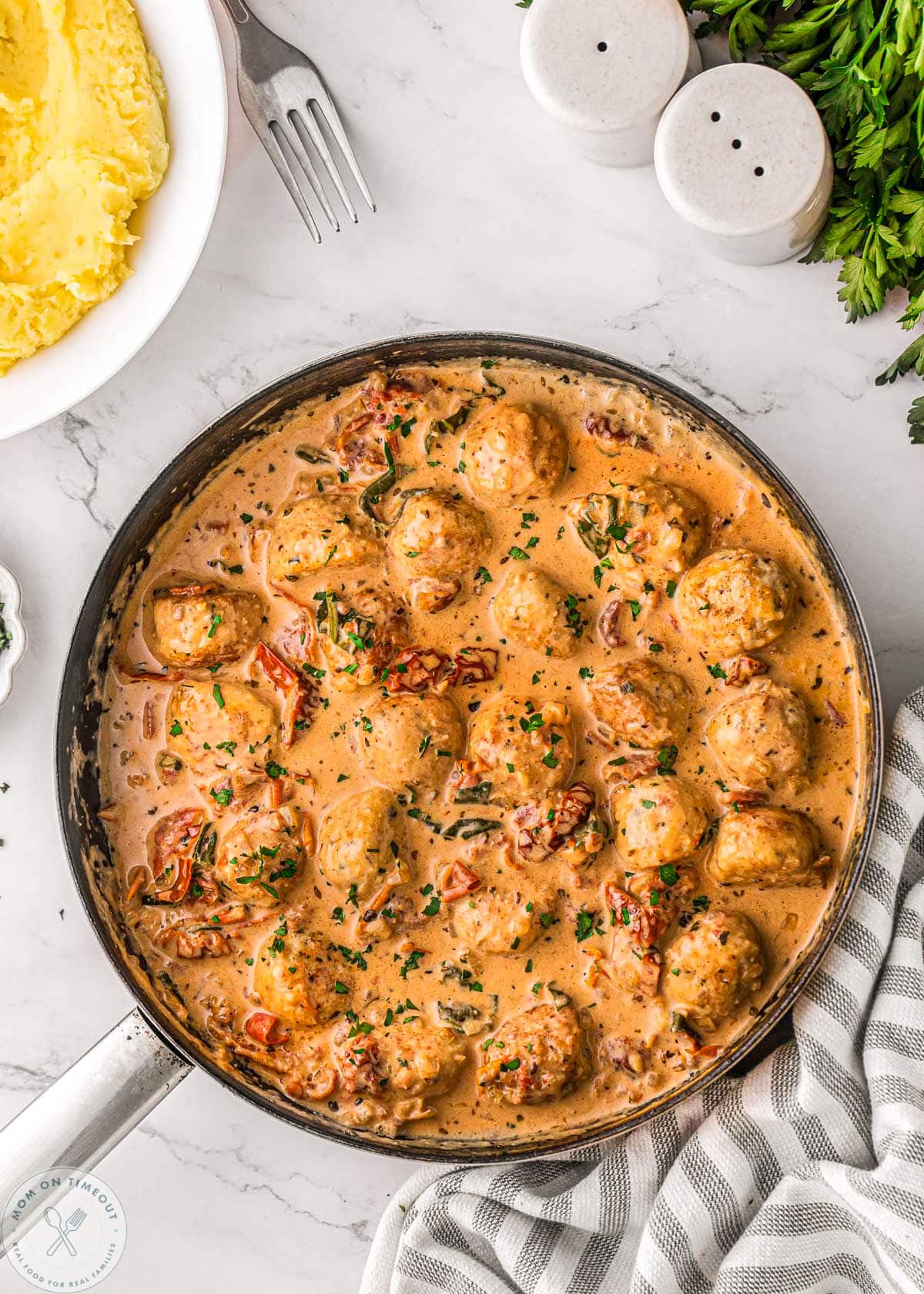 Marry me chicken meatballs in skillet with creamy sun dried tomato and Parmesan sauce. Mashed potatoes in bowl to the side.
