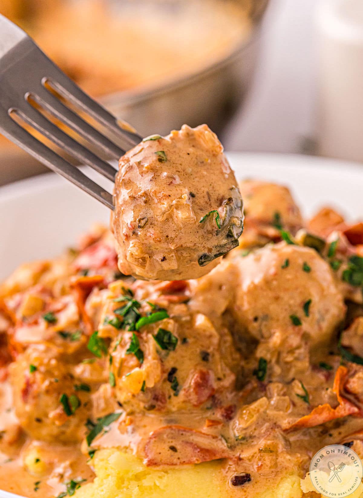 single chicken meatball held on fork above a bowl of more meatballs and mashed potatoes.